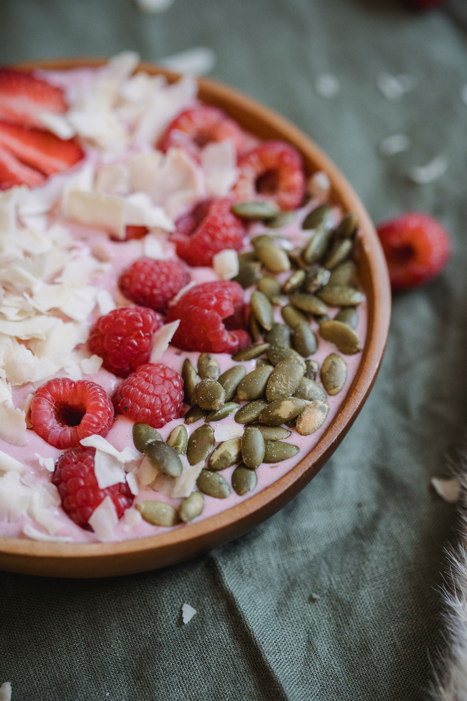 Vegan smoothie bowl topped with raspberries, pumpkin seeds and coconut flakes